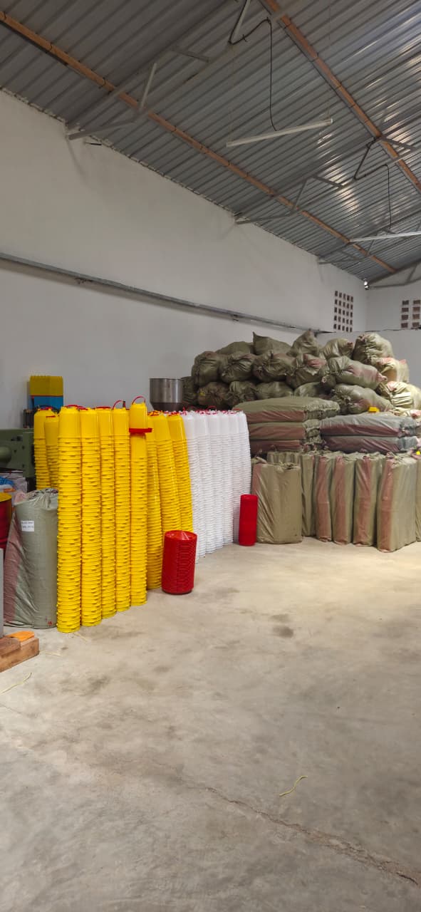 Stacks of newly moulded yellow and white poultry feeders beside sacks of raw polymer at the Fuga factory