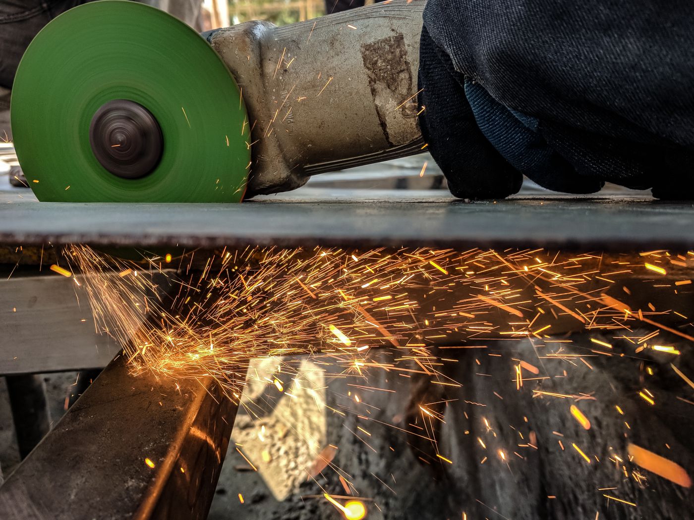 Gloved worker cutting a steel sheet with an angle grinder, sparks streaming from the green cutting disc