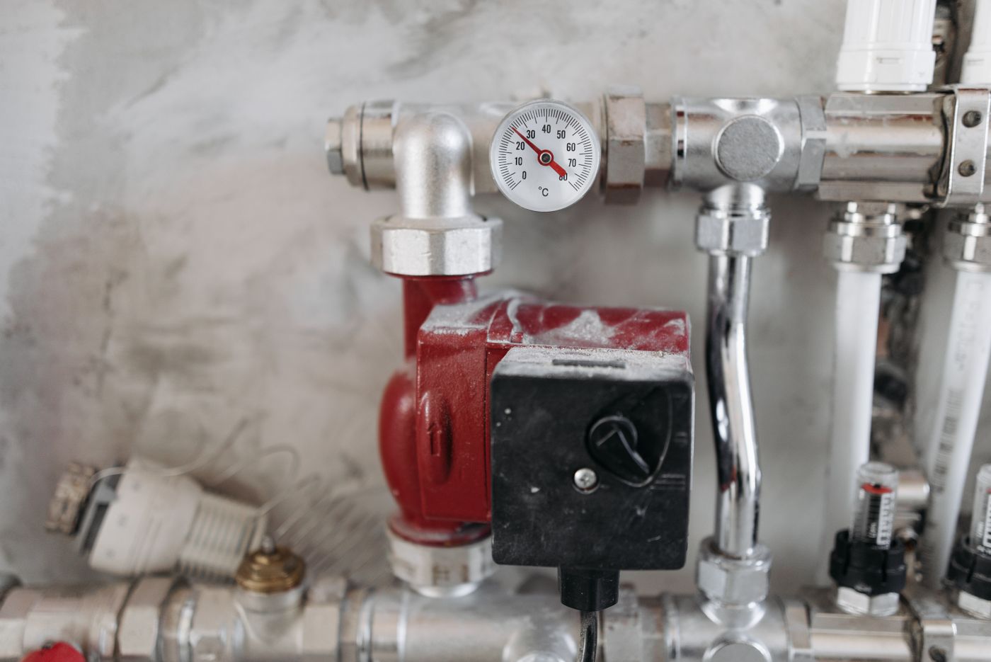 Red inline booster pump plumbed into a domestic water line with a gauge and chrome fittings on a utility room wall