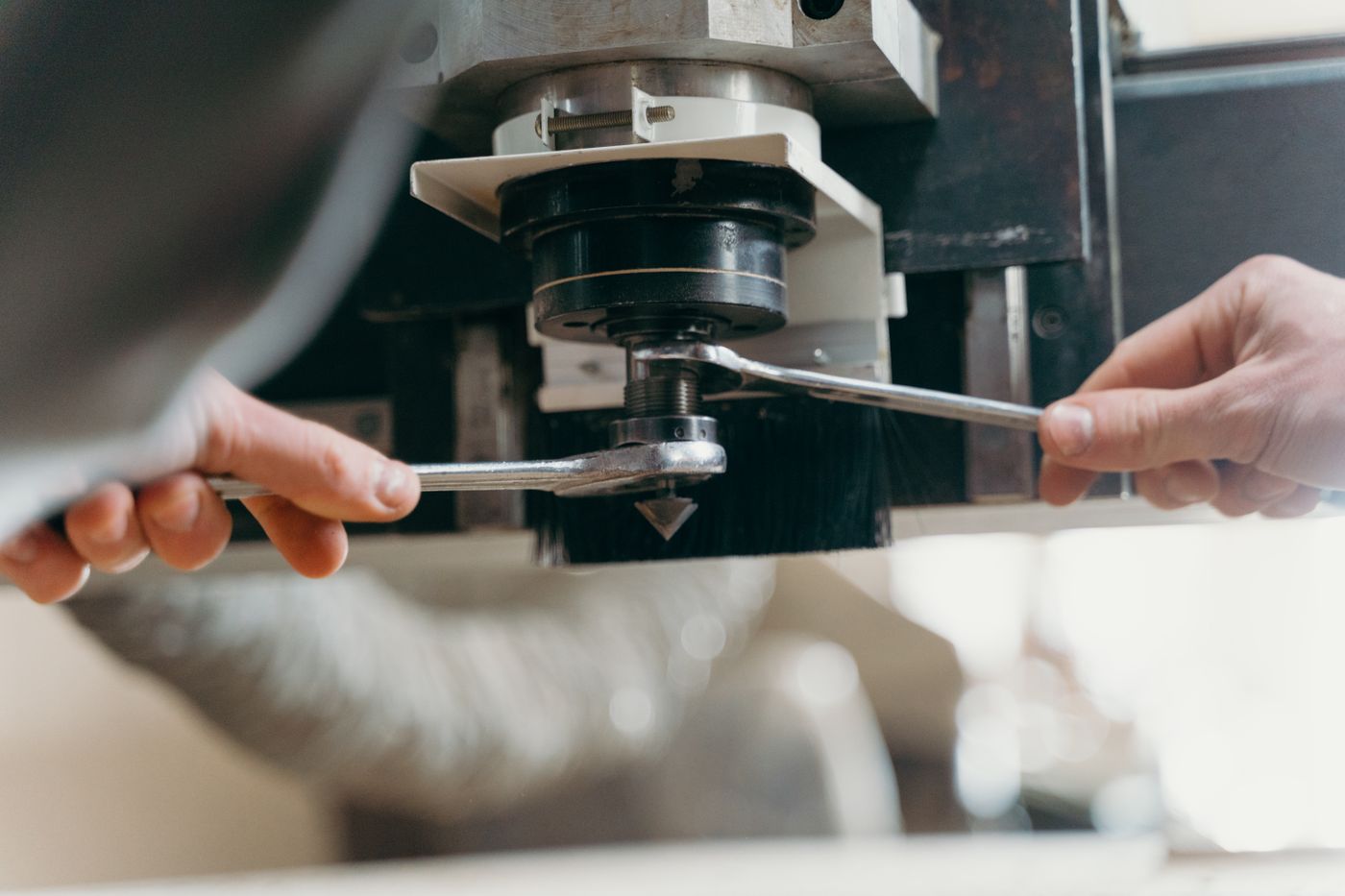 Two hands using open ended spanners to tighten a nut on the shaft of a machine during a service