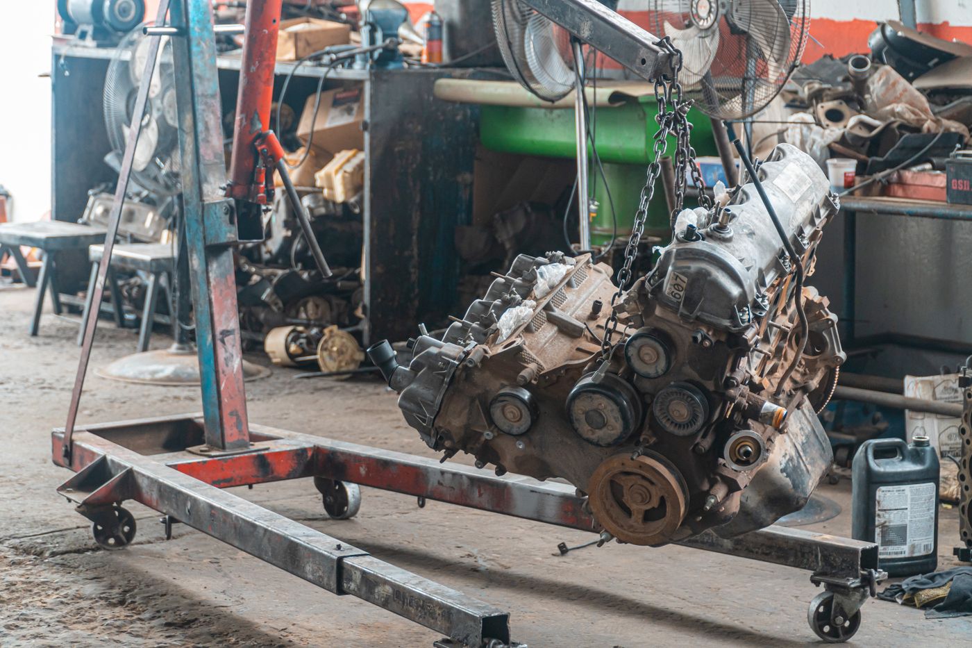 A bare engine hanging from lifting chains on a wheeled engine crane in a mechanical workshop