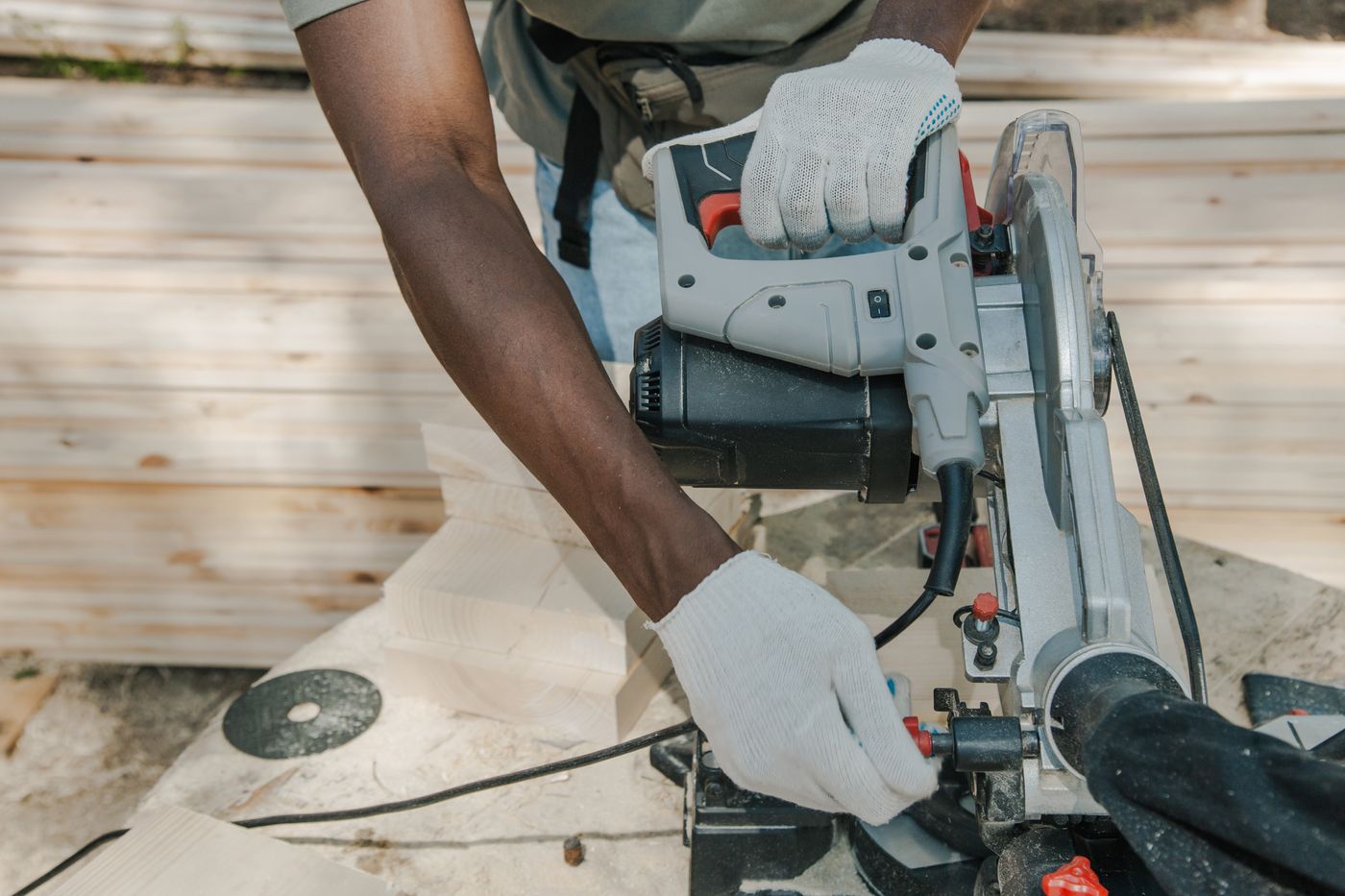 Worker in cotton gloves setting up a circular saw over stacked timber at a bright outdoor work site