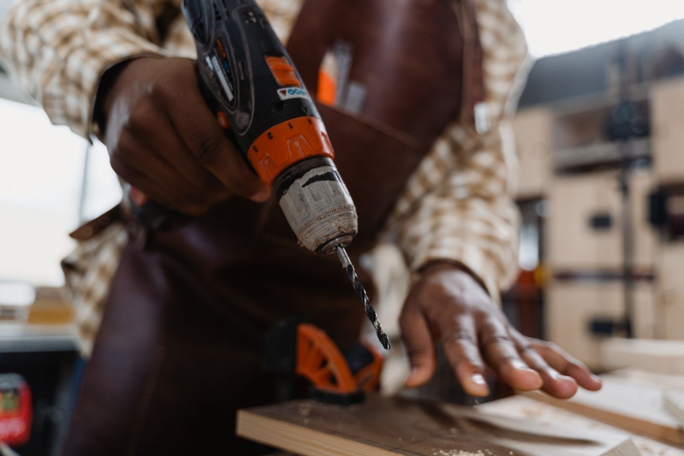 Craftsman drilling into a timber board with a cordless drill on a bright workshop bench