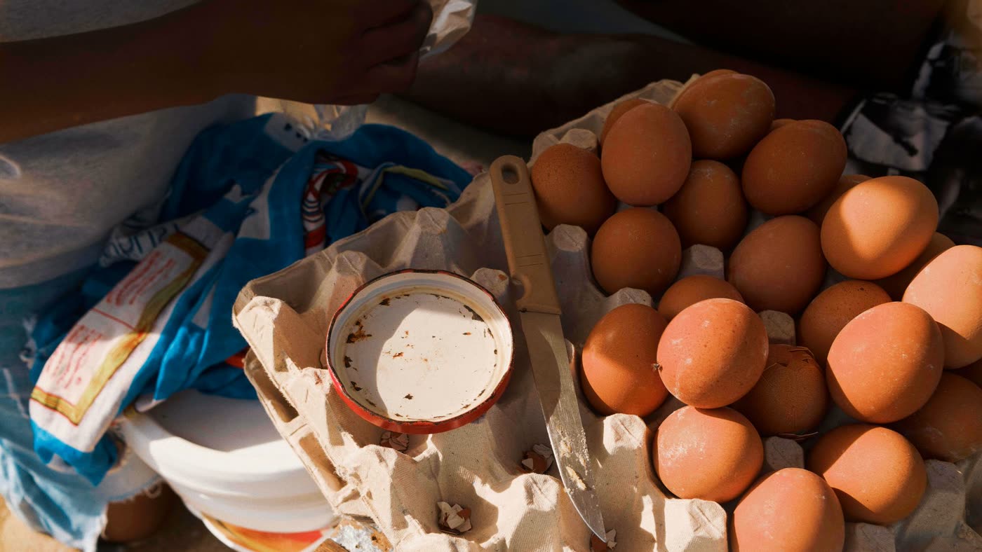 Brown eggs in a cardboard egg tray at a market stall in Luanda, Angola, beside a small tin lid and a kitchen knife