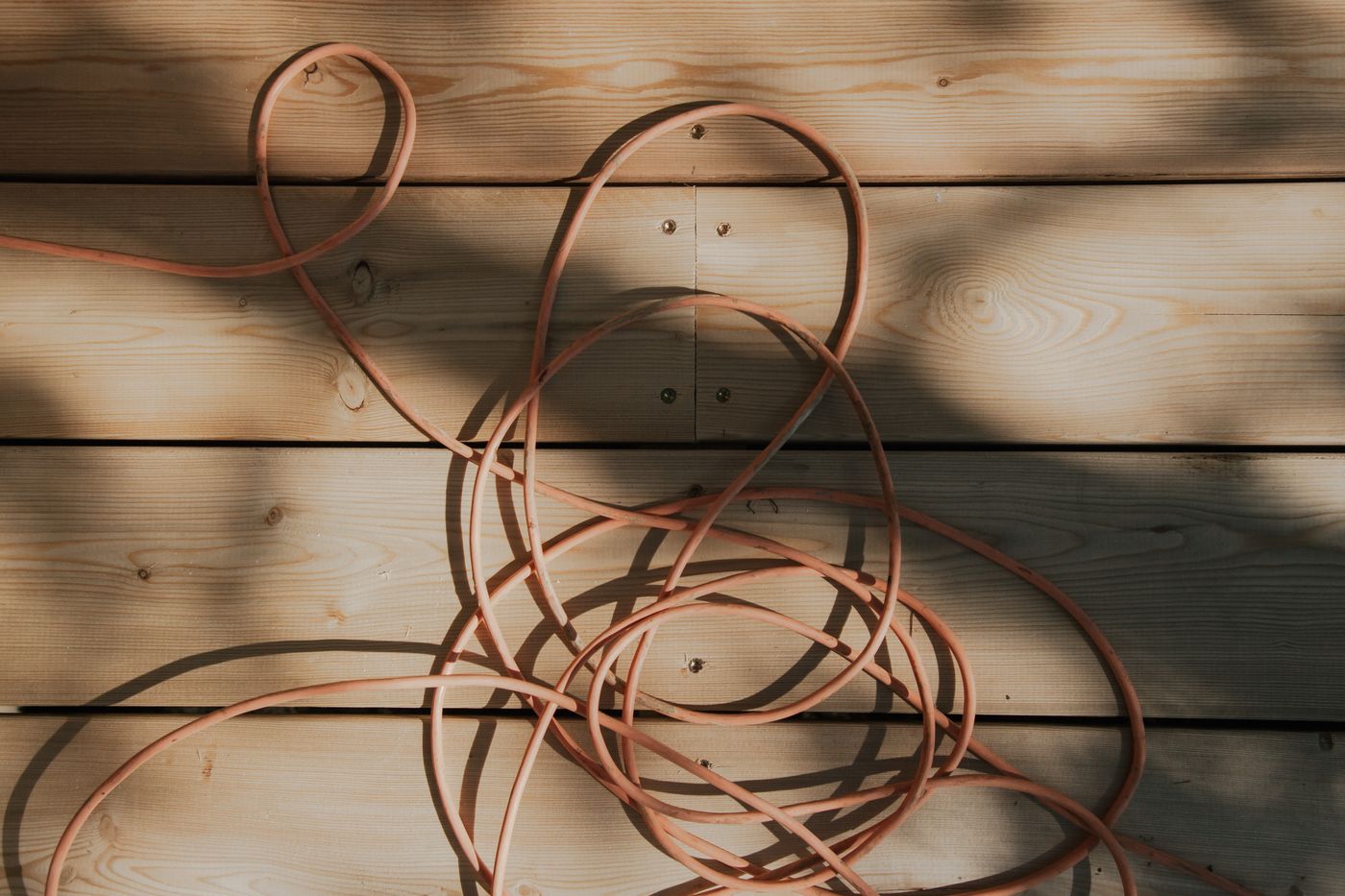 An orange extension cable unwound and lying in loose coils across sunlit timber boards
