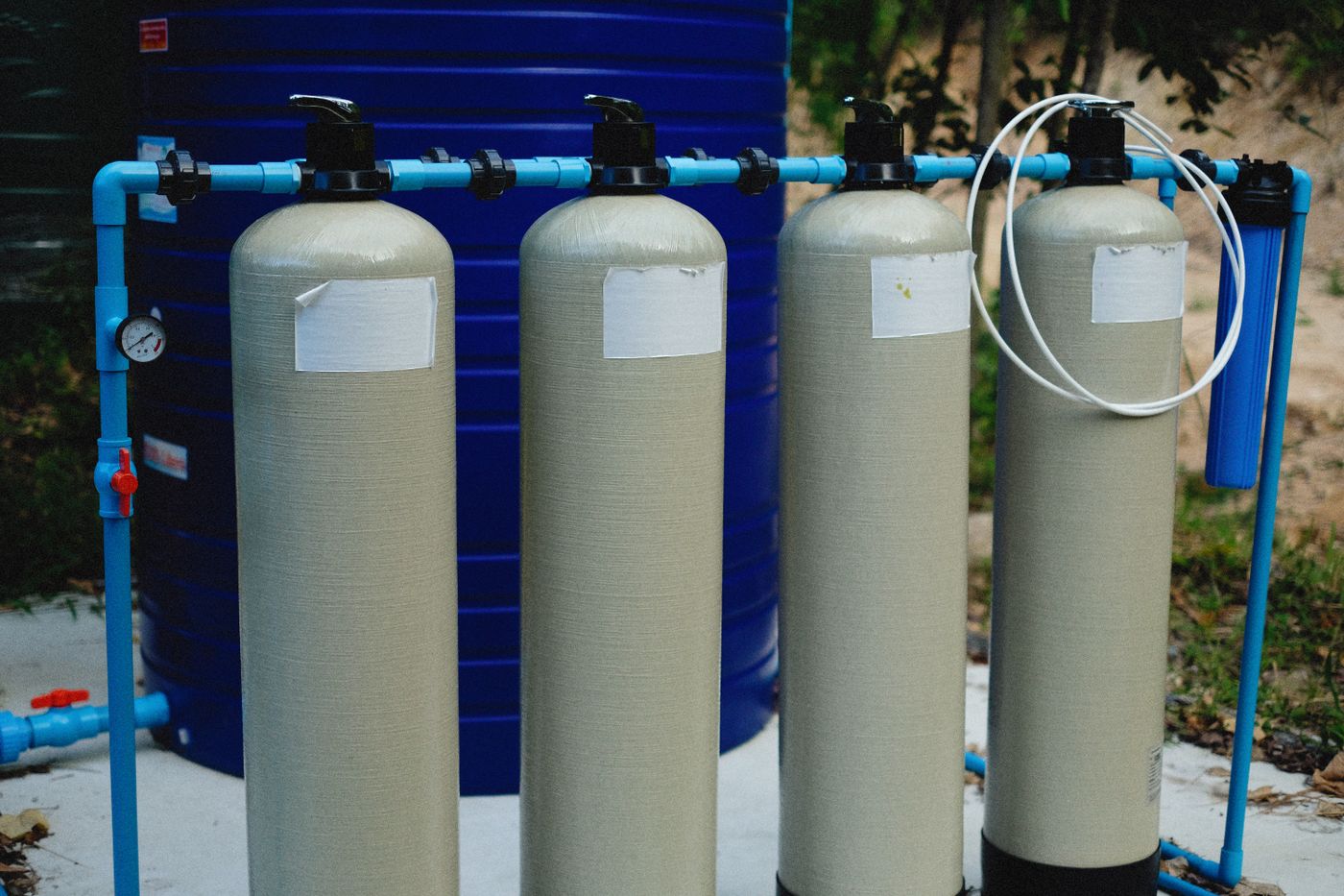 Four fibreglass pressure filter vessels with multiport valves and blue PPR pipework installed beside a plastic storage tank
