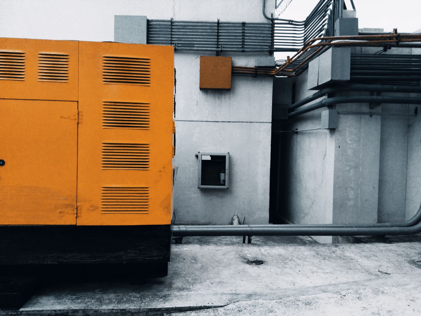 Canopied diesel generator set installed outdoors on a concrete slab beside a wall with exhaust and cable pipework