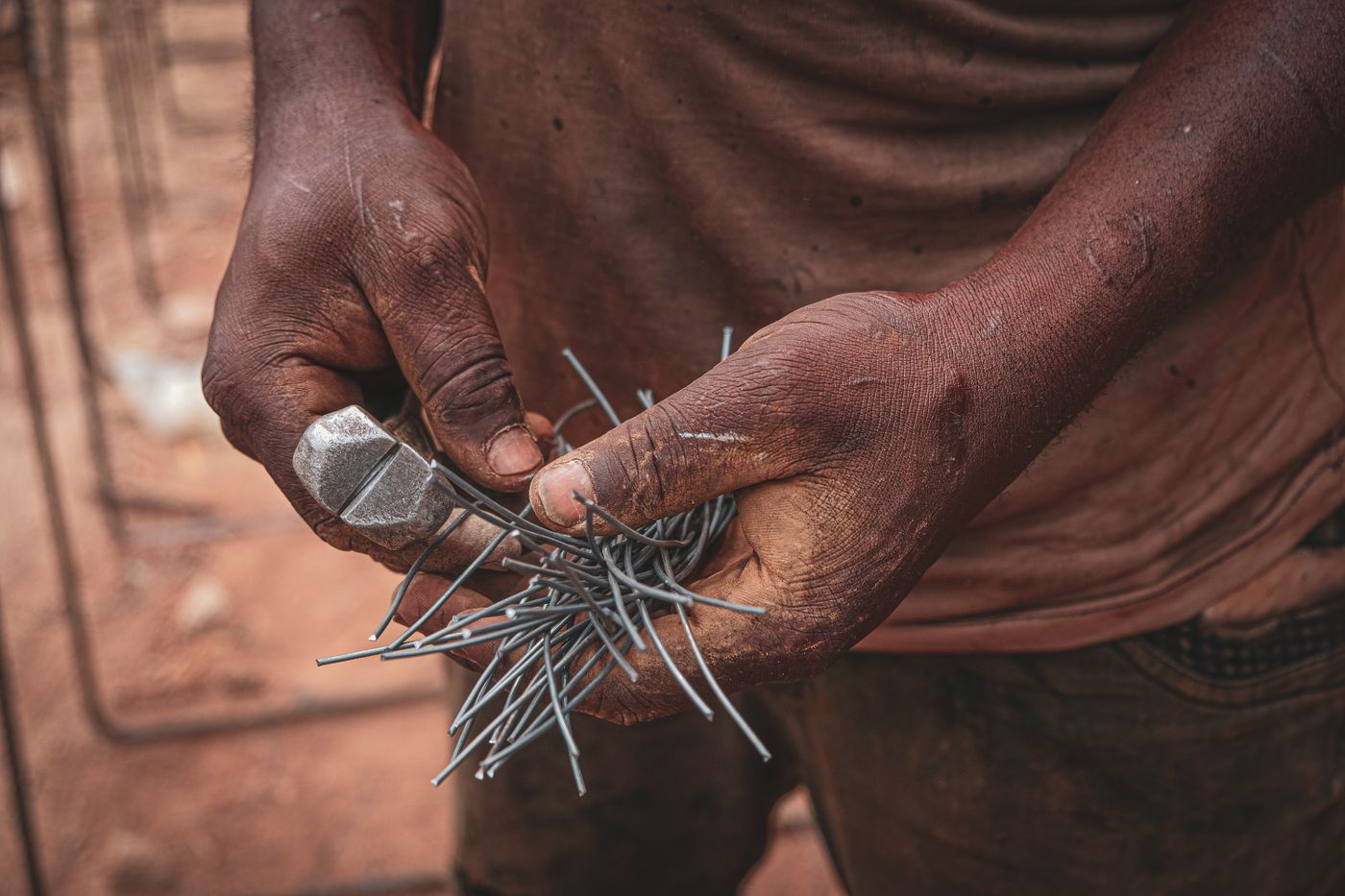 Close-up of a worker's dusty hands holding end cutting pincers and a bundle of cut steel binding wire on a building site with reinforcement bars behind, in Nigeria