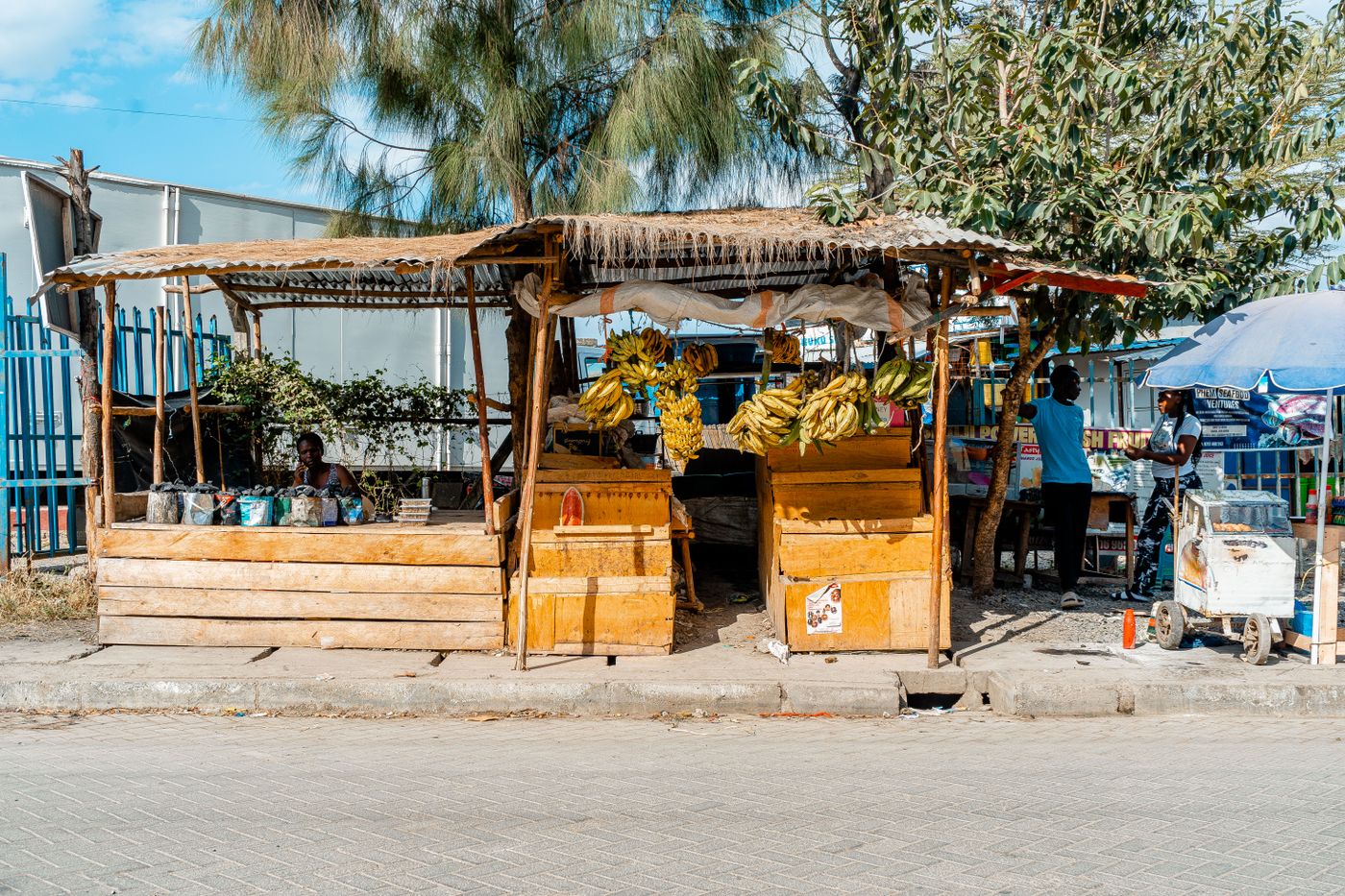 A sunny roadside market on the edge of Nairobi, Kenya with timber vendor stalls and a small trading pitch, the kind of town-edge site where a posho mill is often set up