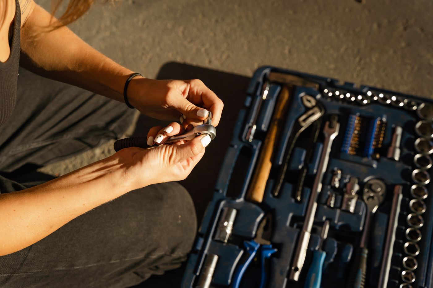 Hands fitting a socket onto a ratchet beside an open socket set case in a sunlit workshop