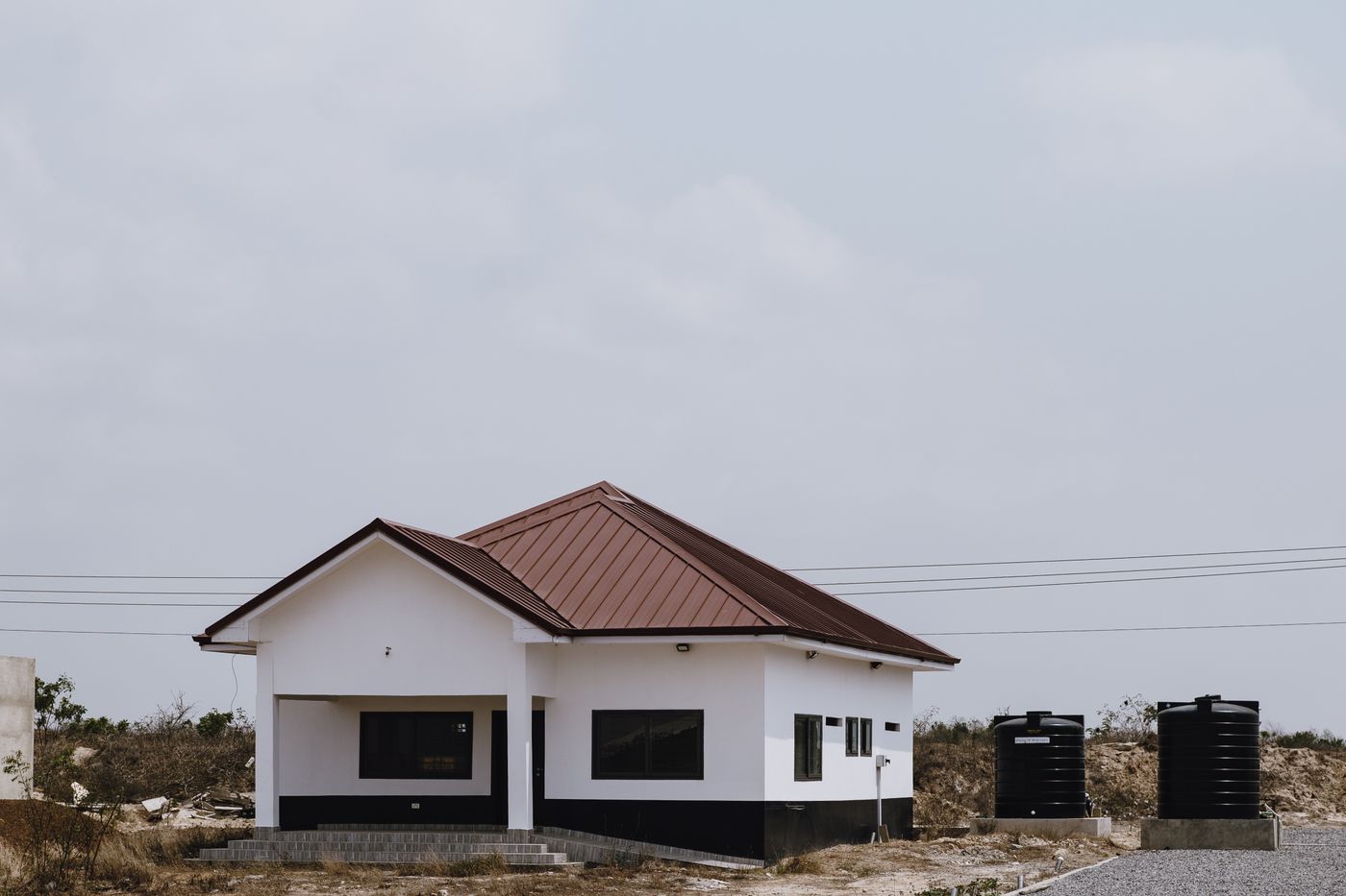Two black plastic water storage tanks standing beside a newly built rural home under a bright sky in Kenya